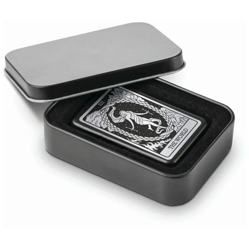May include: A black metal lighter with a silver design of the World tarot card. The lighter is in a black tin box with a black velvet lining.