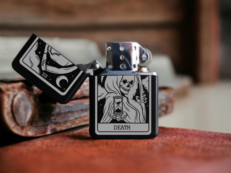 May include: A black lighter with a silver top and a design of the Death tarot card featuring a skeletal figure holding an hourglass. The card reads "DEATH".
