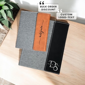 May include: Two personalised leatherette notebook covers. One is grey with a brown leatherette insert with the word "madison" written in cursive. The other is black with a white monogram "DS" with the text "DAVID SMITH" underneath.