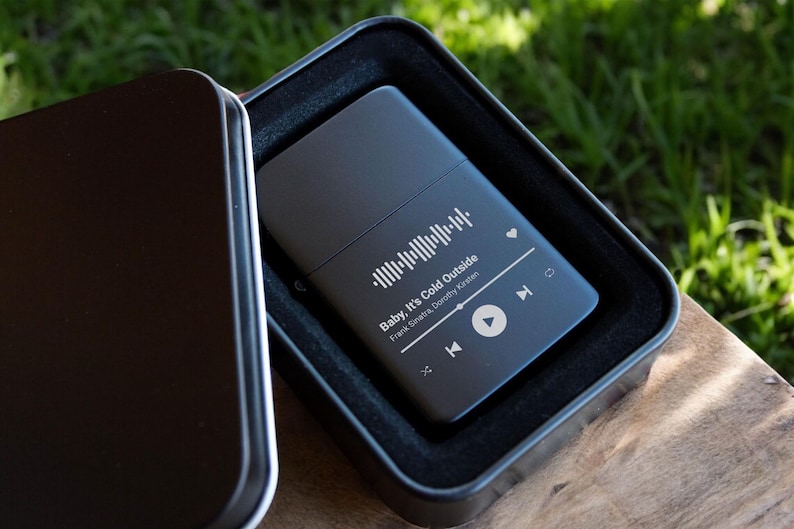 May include: A black metal lighter with a personalized design featuring a song title, artist, and a music player icon. The lighter is in a black gift box.