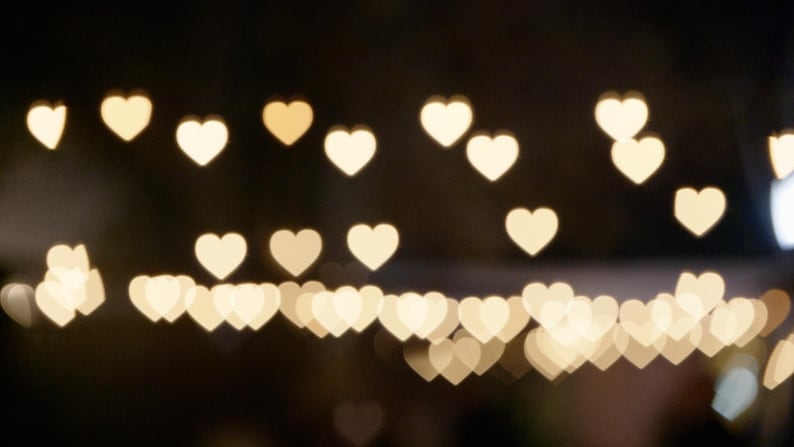 May include: A dark background with a blurred image of many small, white heart shapes.
