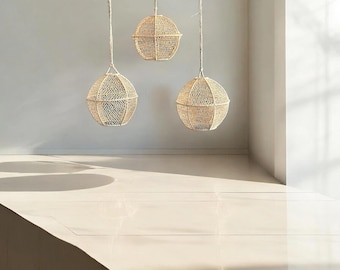 Peut inclure: Trois suspensions sphériques en fibres naturelles tressées sont suspendues au plafond. Les luminaires présentent un design texturé à tissage ouvert et sont suspendus par de fins cordons blanc cassé. Les luminaires sont espacés uniformément, créant une ambiance chaleureuse.