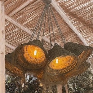 May include: A collection of woven pendant lights with a natural, earthy appearance. Each light has a conical shade in a dark green colour, with a warm, glowing bulb visible inside. The lights are suspended from a central fixture.