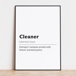 May include: A framed print with the definition of "Cleaner" in bold black text. The definition reads: "Entropy's nemesis armed with lemon-scented justice." The print is in a black frame and hangs on a white wall.