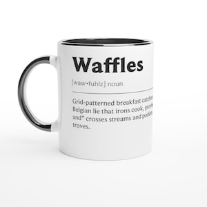 May include: White ceramic mug with a black handle and rim. The mug features the word "Waffles" in bold black letters, along with a definition. A fun and quirky addition to any kitchen or office.