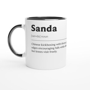 Könnte beinhalten: Weißer Keramikbecher mit schwarzem Henkel und Rand. Der Becher zeigt das Wort "Sanda" in fetter schwarzer Schrift, zusammen mit einer Definition von chinesischem Kickboxen. Die Definition enthält die Aussprache und eine Beschreibung des Sports.