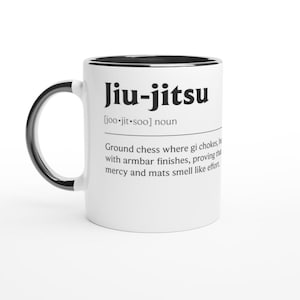Könnte beinhalten: Weißer Keramikbecher mit schwarzem Henkel und Rand. Der Becher zeigt das Wort "Jiu-jitsu" in fetten schwarzen Buchstaben zusammen mit einer Definition. Die Definition beschreibt Jiu-jitsu als "Boden-Schach".