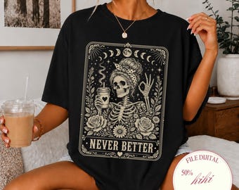 Peut inclure: Un t-shirt noir à manches courtes avec une impression graphique représentant un squelette en chignon tenant une tasse de café. Le motif inclut des éléments floraux, des phases lunaires et le texte "NEVER BETTER" dans un cadre rectangulaire.