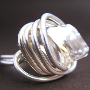Op de afbeelding: Een zilveren ring met een heldere kwartskristal in een draadgewikkeld ontwerp.