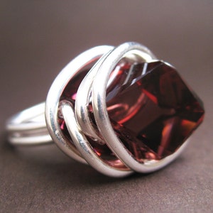 May include: A silver ring with a large, faceted, dark red gemstone set in a wire-wrapped design.