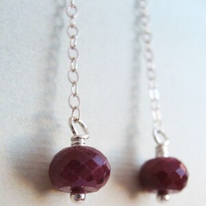 May include: A pair of silver dangle earrings with a deep red gemstone on each. The gemstones are faceted and have a shiny finish.