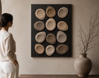 May include: A rectangular black wall art piece featuring twelve circular, textured, tan and beige woven fiber elements arranged in a grid. The circular forms have a concave center and are mounted on a flat, dark, solid-colored rectangular panel.