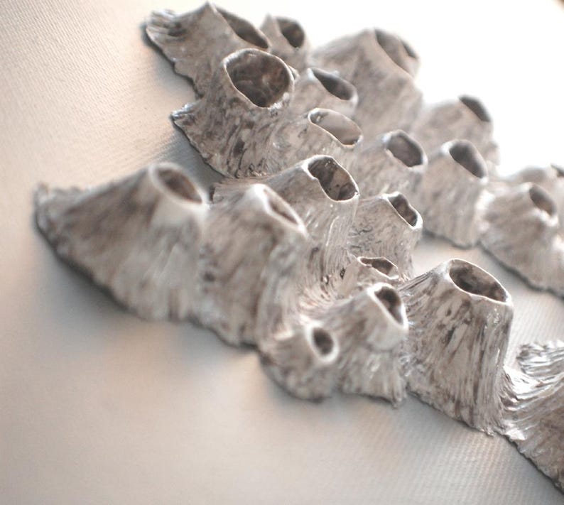 Puede incluir: Una escultura de cer&aacute;mica blanca con una superficie texturizada que se asemeja al coral. La escultura tiene m&uacute;ltiples formas redondeadas y huecas, creando un dise&ntilde;o &uacute;nico y org&aacute;nico.