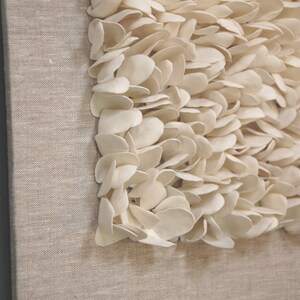 May include: A close-up of a beige canvas wall art piece with a textured design of white, petal-like shapes.