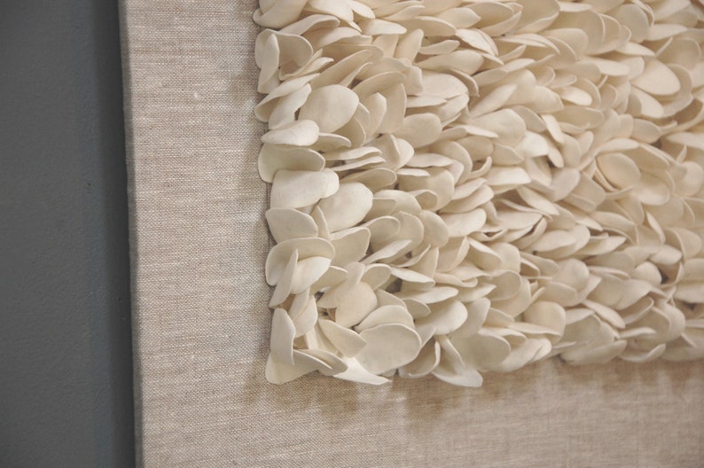 May include: A close-up of a beige canvas wall art piece with a textured design of white, petal-like shapes.