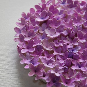 May include: A close-up of a circular arrangement of purple paper flowers. The flowers are all the same size and shape, and they are arranged in a tight circle. The flowers are made of paper and have a slightly textured surface.