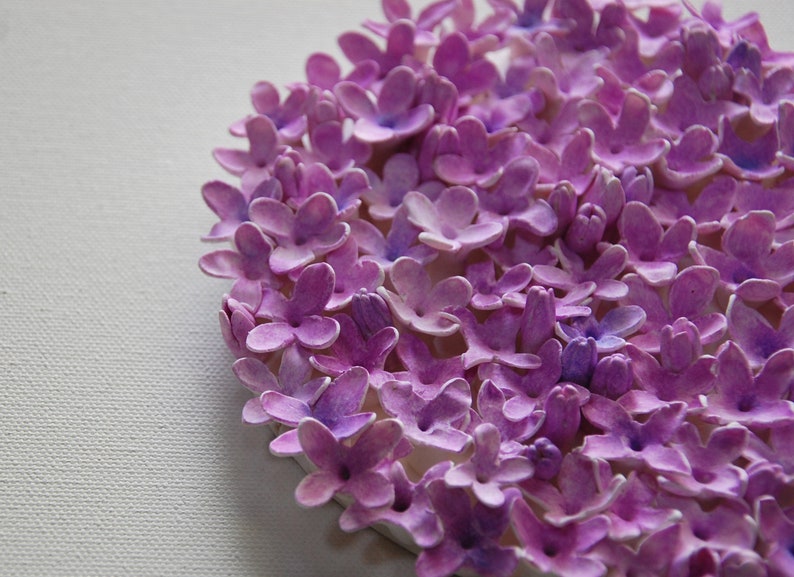 May include: A close-up of a circular arrangement of purple paper flowers. The flowers are all the same size and shape, and they are arranged in a tight circle. The flowers are made of paper and have a slightly textured surface.