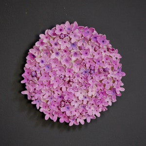 May include: A close-up of a round arrangement of small, pink and purple flowers. The flowers are densely packed together, creating a circular shape.