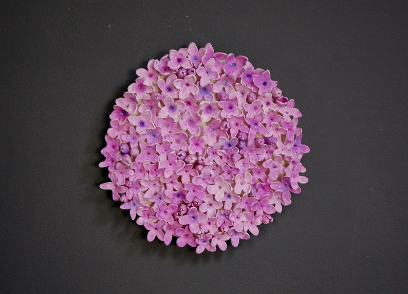 May include: A close-up of a round arrangement of small, pink and purple flowers. The flowers are densely packed together, creating a circular shape.