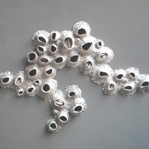 Puede incluir: Una escultura de metal de color plateado que representa un arrecife de coral con muchos agujeros peque&ntilde;os y una superficie texturizada.