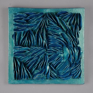 May include: Teal blue square wall art with a textured, abstract design. The design is made up of many small, overlapping shapes that create a sense of depth and movement.