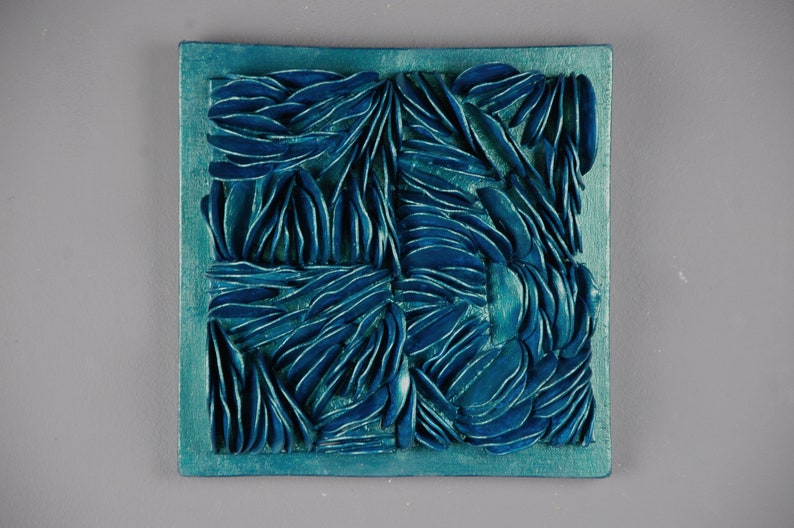 May include: Teal blue square wall art with a textured, abstract design. The design is made up of many small, overlapping shapes that create a sense of depth and movement.