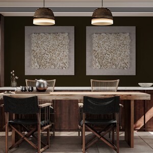 May include: A dining room with a wooden table and chairs. The table has a white marble top and a wooden base. There are two black chairs with wooden frames and a woven chair with a wooden frame. The walls are painted a dark brown color and there are two white framed pictures on the wall. There is a bookshelf on the right side of the image.