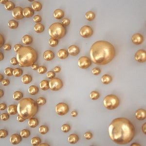 Könnte beinhalten: Eine weiße Oberfläche, die mit goldfarbenen runden Ornamenten in verschiedenen Größen bedeckt ist.