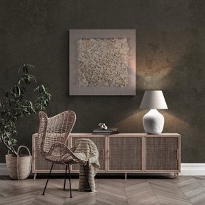 May include: A wicker chair with a throw blanket sits in front of a wooden cabinet with woven doors. A lamp with a white shade sits on the cabinet. A framed abstract art piece hangs on the wall behind the cabinet.