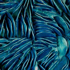May include: A close-up of a textured blue surface made of overlapping, curved shapes. The surface has a metallic sheen and a slightly iridescent quality.