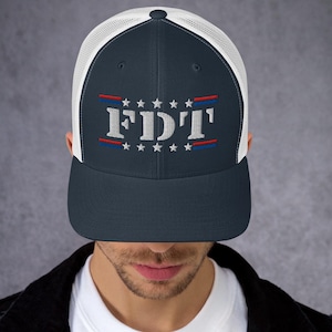 May include: Navy blue trucker hat with white mesh backing. The front of the hat features the embroidered text "FDT" in white, with red and blue accents and a row of white stars.