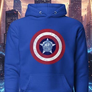 Puede incluir: Una sudadera con capucha azul real con un dise&ntilde;o de escudo en la parte delantera. El escudo tiene un patr&oacute;n circular rojo y blanco con un emblema central. La sudadera tiene un bolsillo de canguro y una capucha con cord&oacute;n.