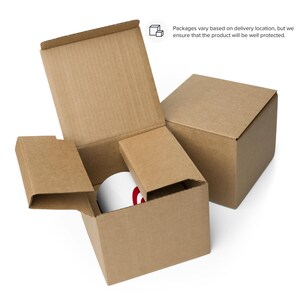 May include: A white mug with a red design is nestled inside a brown cardboard box with protective inserts. The box is open, revealing the mug, and is placed next to a closed box. Text on the image states, "Packages vary based on delivery location, but we ensure that the product will be well protected."