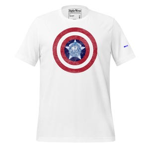 May include: White t-shirt featuring a distressed red and white shield design with a blue and white star emblem at the center. The shirt has short sleeves and the text "Alpha Wear" is printed on the tag.