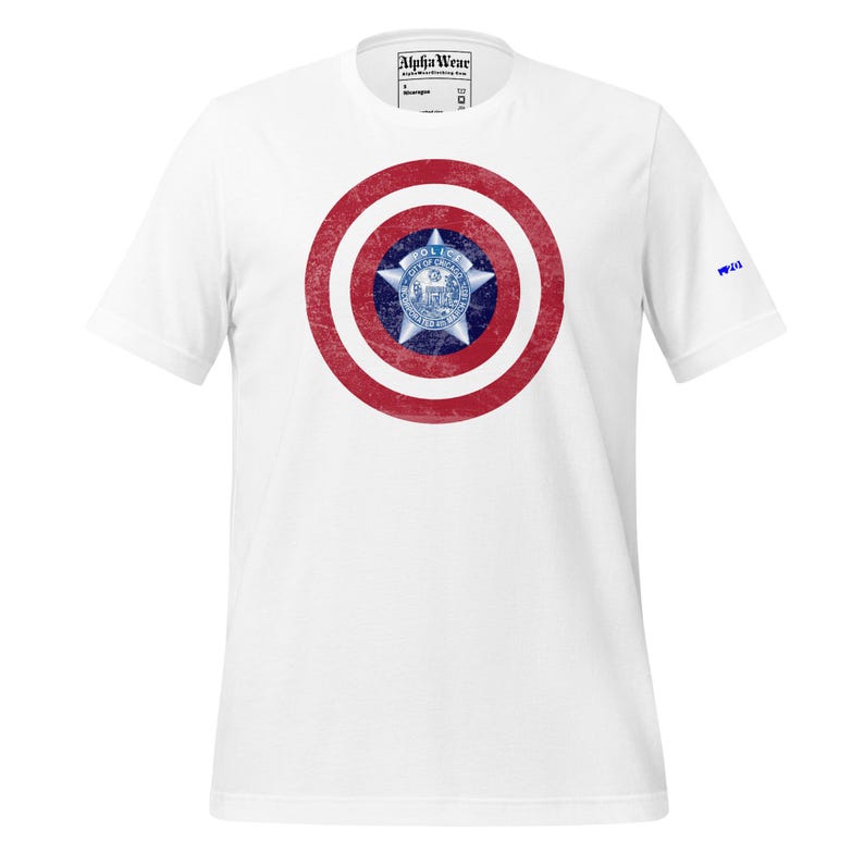 May include: White t-shirt featuring a distressed red and white shield design with a blue and white star emblem at the center. The shirt has short sleeves and the text "Alpha Wear" is printed on the tag.