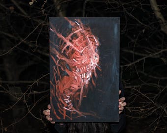 May include: A rectangular canvas art piece featuring a red, abstract, and grotesque face against a dark background. The artwork has a textured appearance with visible brushstrokes, creating a sense of depth and intensity. The painting is held in front of a dark, natural backdrop.