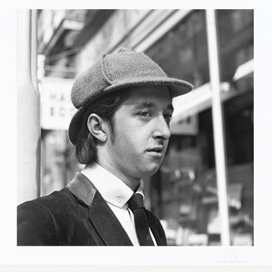 May include: A black and white photograph of a man wearing a tweed hat and a suit jacket. He is looking to the right of the frame.