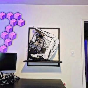 May include: A white and black computer case with a geometric design is mounted on a wall shelf. The case is tilted at an angle, and the interior components are visible. The shelf is black and has a white background.