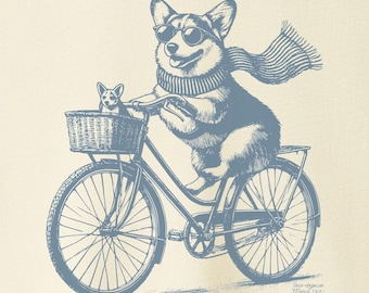 May include: A light beige t-shirt with a blue illustration of a corgi riding a bicycle with a smaller corgi in the basket. The corgi is wearing sunglasses and a scarf.
