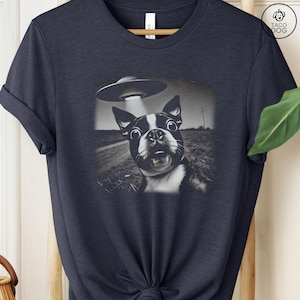 May include: A navy blue t-shirt with a black and white image of a Boston Terrier looking up at a UFO. The dog has a surprised expression on its face.