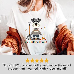 May include: White t-shirt with a cartoon image of a small dog wearing a sweater and holding a rake. The dog is surrounded by autumn leaves. The text "Life is better with a dog." is printed below the image.