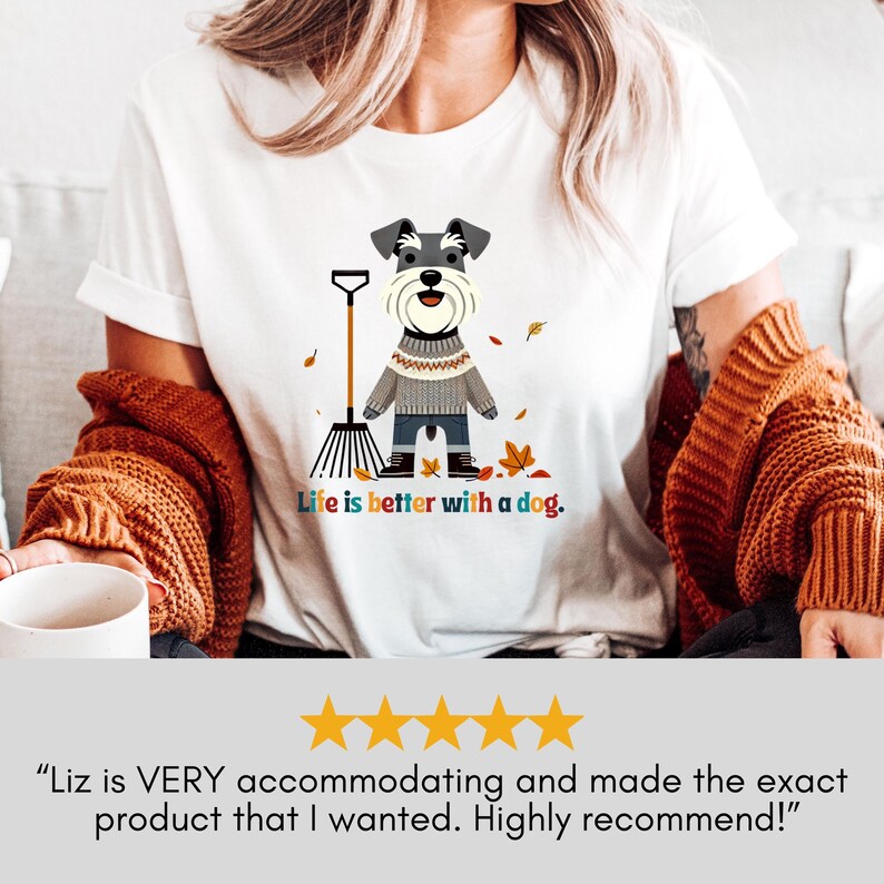 May include: White t-shirt with a cartoon image of a small dog wearing a sweater and holding a rake. The dog is surrounded by autumn leaves. The text "Life is better with a dog." is printed below the image.