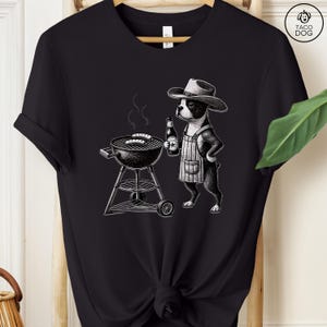 Peut inclure: Une illustration en noir et blanc d'un Boston Terrier portant un chapeau de cowboy et un tablier, faisant griller des saucisses sur un barbecue au charbon de bois. Le chien tient une bouteille de bi&egrave;re dans une patte.