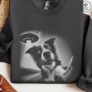 May include: A black and white image of a dog looking up at a UFO. The dog has a surprised expression on its face. The UFO is a classic flying saucer shape.
