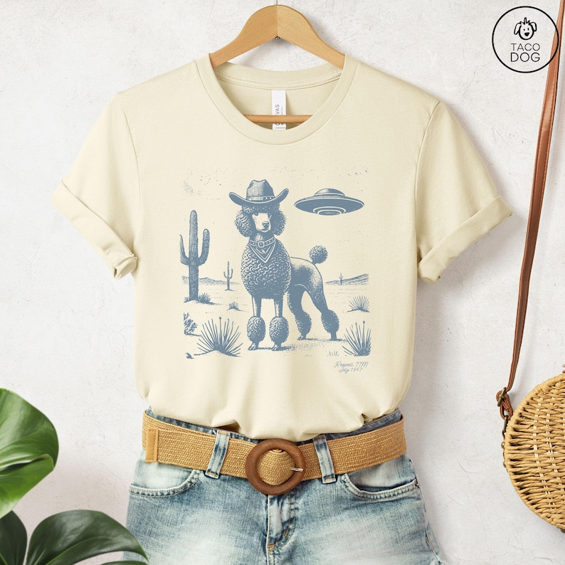 a t-shirt with an illustration of a poodle wearing a cowboy hat with a ufo in the background