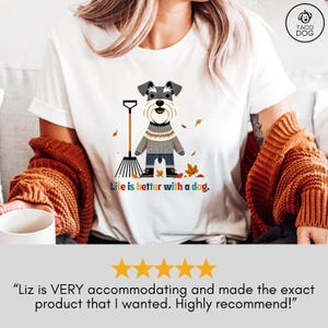 May include: White t-shirt with a cartoon illustration of a small gray dog wearing a sweater and holding a rake. The dog is surrounded by colorful autumn leaves. The text "Life is better with a dog." is printed below the dog.
