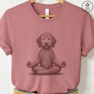 May include: Dusty rose t-shirt featuring a detailed illustration of a dog in a meditative pose. The dog is depicted with closed eyes and crossed legs, hands resting on knees. The shirt has a crew neck and short sleeves. The brand logo "TACO DOG" is visible.
