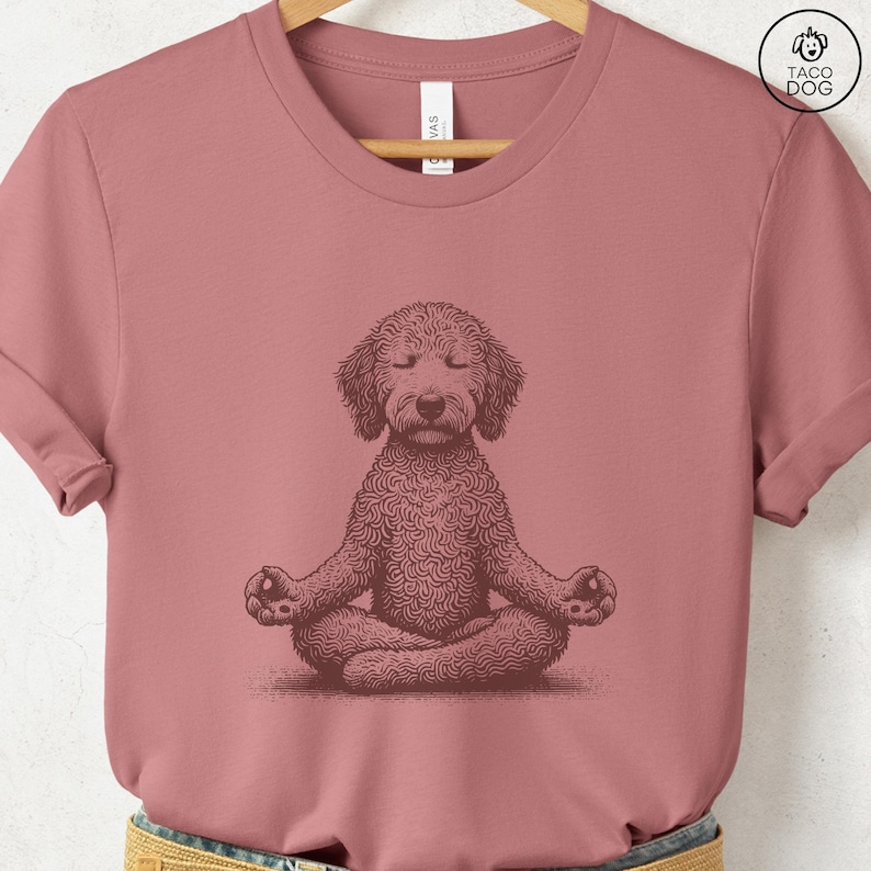 May include: Dusty rose t-shirt featuring a detailed illustration of a dog in a meditative pose. The dog is depicted with closed eyes and crossed legs, hands resting on knees. The shirt has a crew neck and short sleeves. The brand logo "TACO DOG" is visible.