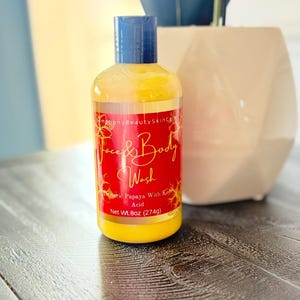 Puede incluir: Una botella transparente de gel limpiador facial y corporal con líquido amarillo. La etiqueta roja tiene texto dorado que dice "Face & Body Wash" y "Tumeric Papaya With Kojic Acid". La botella tiene una tapa azul y pesa 274g.