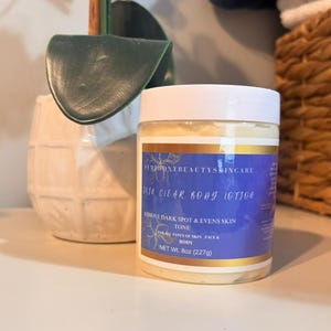 May include: A clear plastic jar of Skin Clear Body Lotion with a white lid. The label is blue and gold, with text that reads "Remove Dark Spot & Evens Skin Tone". The jar contains 8 oz (227g) of lotion.